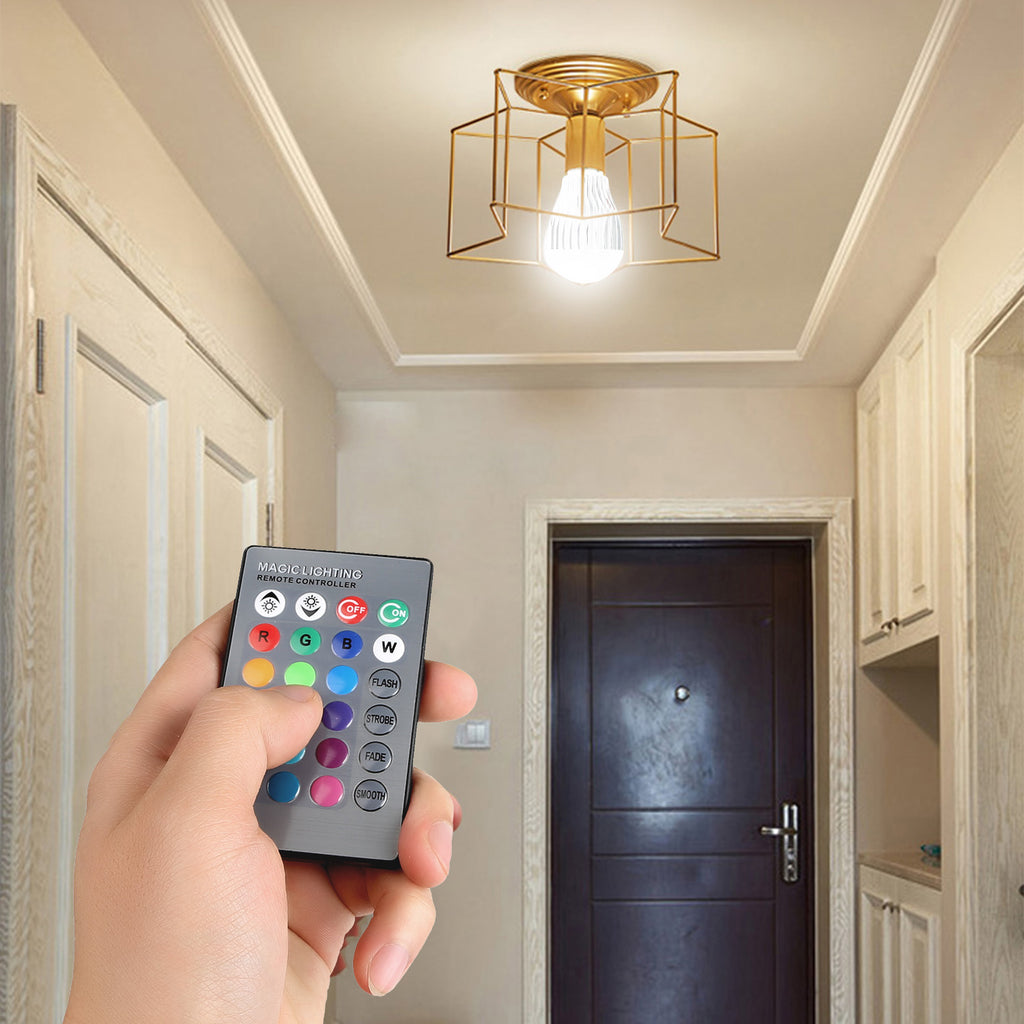 Hand holding a remote control with a ceiling light fixture in a hallway.