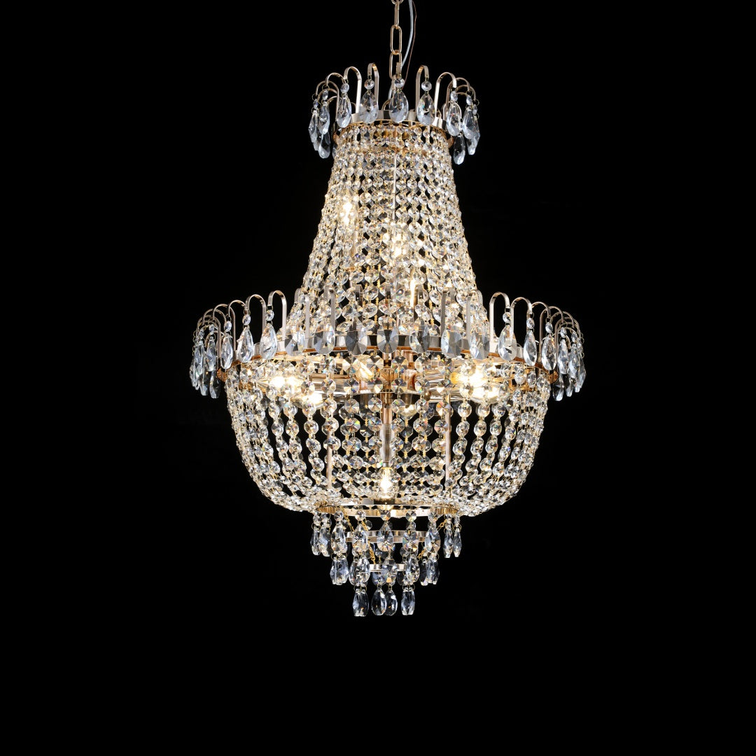 A multi-tiered crystal chandelier with gold-toned metal frames and hanging clear glass prisms, shown illuminated against a solid black background.