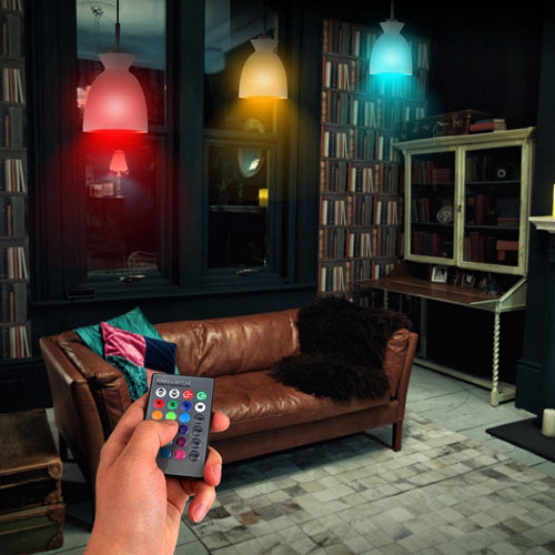 Hand holding a remote control in a dimly lit room with a brown leather sofa and bookshelves.