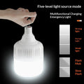 An illuminated white emergency lantern with a metal hanging loop, shown with a hand interacting with the top connector. The image includes text describing 'Five-level light source mode' and a side panel showing light intensity levels labeled Strong light, Normal Light, Weak light, Flash Mob, and Slow Flash, all on a black background.